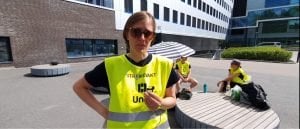 Kvinne i Unio-streikevest foran sittende streikevakt og en stor offentlig bygning